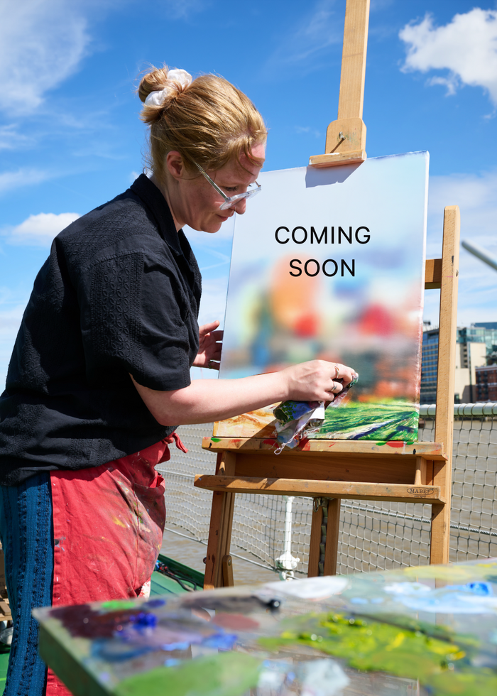 Person painting outdoors with a 'Coming Soon' sign in the background